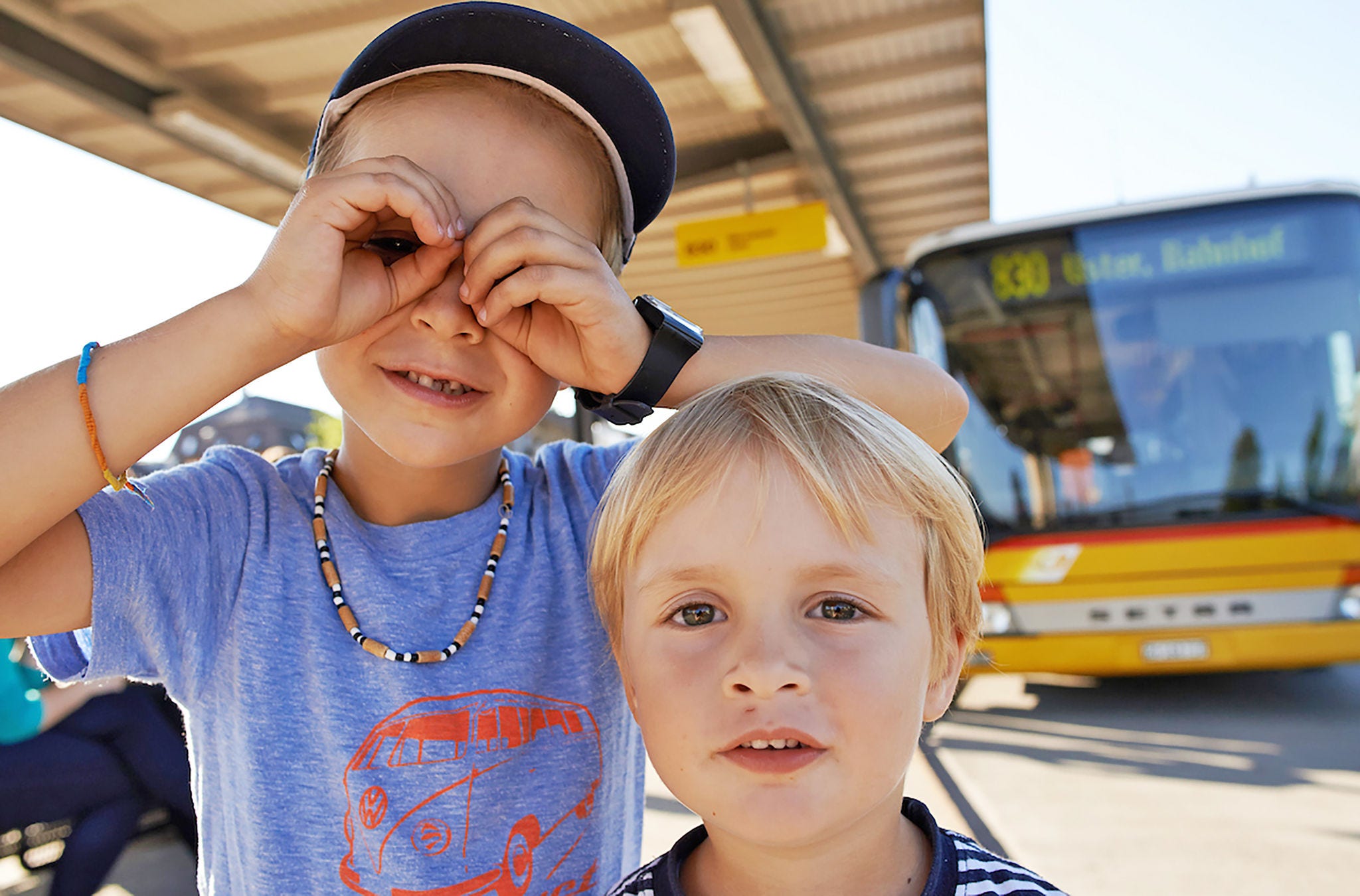 Zwei Buben vor dem PostAuto am Bahnhof.